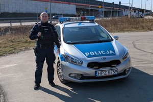 Zdjęcie przedstawia umundurowanego policjanta przy radiowozie.