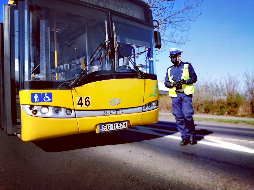 Zdjęcie kolorowe: policjant ruchu drogowego w trakcie działań związanych ze zwalczaniem covid-19 przechodzi obok autobus podczas jego kontroli