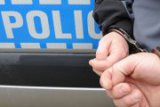 Męskie dłonie zapięte w kajdanki na tle napisu Policja