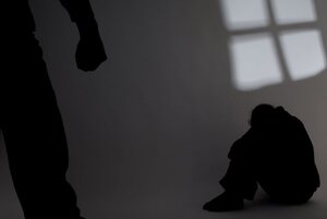 Cień osoby skulonej w kącie pokoju i cień dłoni zaciśniętej w pięść