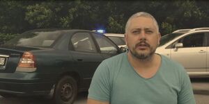 Mężczyzna siedzący na wózku inwalidzkim na tle dwóch rozbitych samochodów