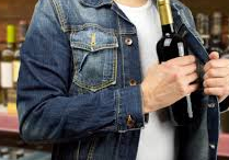 Mężczyzna wkładający za kurtkę butelkę alkoholu