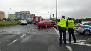 Zdjęcie kolorowe: Aleja Wojciech Korfantego na drodze rozbite dwa samochody osobowe na tle policyjnego radiowozu i wozu bojowego straży pożarnej, z prawej strony dwóch policjantów zabrzańskiej drogówki koło policyjnego radiowozu