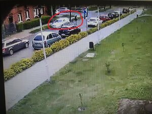 Zdjęcie kolorowe: obraz z monitoringu: ulica z zaparkowanymi samochodami i mężczyzna, który kierował srebrnym samochodem osobowym