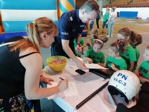 Zdjęcie kolorowe: zabrzański policjant na hali MOSiR z dzieckiem i jego wychowawczynią odciskają ślady daktyloskopijne