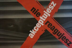 Zdjęcie kolorowe: plakat kampania społecznej "Nie reagujesz - akceptujesz" - oko człowieka wyglądające z pomiędzy rozszerzonych żaluzji