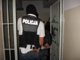 Zdjęcie kolorowe: policjant kryminalny w kamizelce taktycznej z napisem policja wprowadzający do policyjnego aresztu osobę zatrzymaną