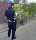 Zdjęcie kolorowe: policjantka zabrzańskiej drogówki podczas wypełniania dokumentacji z wypadku drogowego stojąca na chodniku przy rowerze