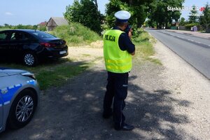 Zdjęcie kolorowe: policjant dokonuje pomiaru prędkości na drodze.