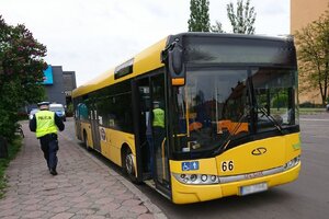 Zdjęcie kolorowe: żółty autobus komunikacji miejskiej i policjant ruchu drogowego, w tle policyjny radiowóz