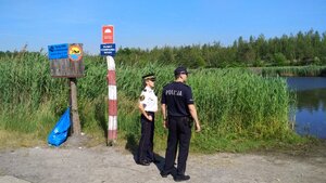 Zdjęcie kolorowe: policjant i strażnik miejski kontrolują zbiornik wodny.