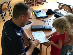 Zdjęcie kolorowe: policjant podczas prelekcji daje dziecko kolorowankę.
