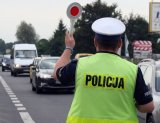 Zdjęcie kolorowe: policjant drogówki podczas działań z tarczą do zatrzymywania pojazdów