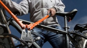 zdjęcie kolorowe: mezczyzna, który przy pomocy narzędzi przecina zabezpieczenie roweru