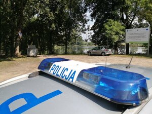 Zdjęcie kolorowe: policyjny radiowóz przy zbiorniku wodnym.