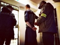 Zdjęcie kolorowe: policjanci operacyjni zakładają kajdanki zatrzymanemu