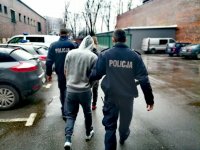 Zdjęcie kolorowe: policjanci prowadzą zatrzymanych mężczyzn przez parkin policyjny