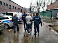 Zdjęcie kolorowe: policjanci prowadzą zatrzymanych mężczyzn przez parkin policyjny