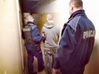 Zdjęcie kolorowe: policjanci prowadzą zatrzymanego przez korytarz w pomieszczeniach dla osób zatrzymanych