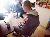 Zdjęcie kolorowe: policjanci operacyjni rozpytują zatrzymanego, który siedzi na  krześle skuty kajdankami