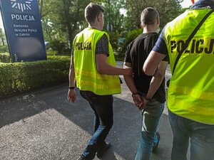 Zdjęcie kolorowe: policjanci doprowadzają zatrzymanego mężczyznę na czynności
