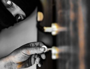 Zdjęcie kolorowe: zamaskowana postać otwiera zamek w drzwiach.