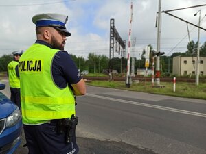 Zdjęcie kolorowe: Policjant obserwuje rejon przejazdu kolejowego