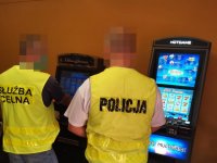 Zdjęcie kolorowe: Nieumundurowany Policjant oraz funkcjonariusz Służby Celno-Skarbowej podczas wykonywania czynności służbowych w związku z zabezpieczeniem nielegalnych automatów do gier hazardowych