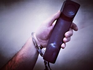 Zdjęcie kolorowe: ręka trzymająca słuchawkę  telefonu w kajdankach