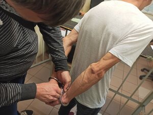 Zdjęcie kolorowe: podejrzany o stalking w pomieszczeniach dla osób zatrzymanych prowadzony przez policjantów.