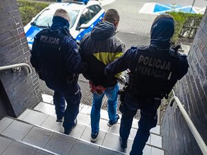 Zdjęcie kolorowe: umundurowani policjanci prowadza zatrzymanego mężczynę