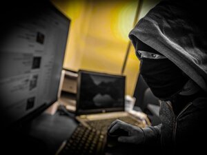 Zamaskowana osoba z kapturem na głowie  przed monitorem