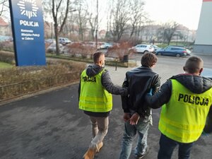 Policjanci ubranie w kamizelki odblaskowe doprowadzaj zatrzymanego na czynności
