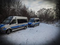 Policyjne radiowozy mercedes sprinter zaparkowane w terenie porośniętym zaroślami przy zimowej pogodzie.