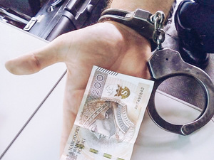ręką z założonymi kajdankami i banknotem