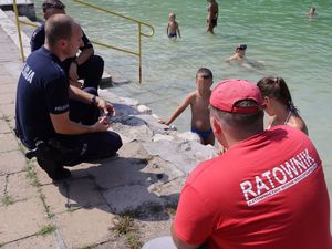 Zdjęcia kolorowe: Umundurowani policjanci wspólnie z ratownikami Wodnego Ochotniczego Pogotowia Ratunkowego, na terenie Kąpieliska Leśnego rozmawiają z dziećmi i młodzieżą na temat bezpieczeństwa nad wodą.