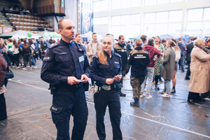 Policjanci zabrzańskiej komendy na targach edukacyjnych idą przez  hale wśród uczestników targów