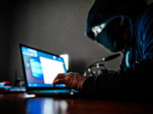 Zamaskowana osoba używająca laptopa.
