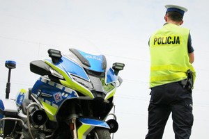 Zdjęcie kolorowe przedstawiające umundurowanego policjanta stojącego obok policyjnego motocykla.