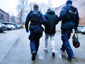 Na zdjęciu policjanci prowadzą zatrzymanego