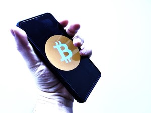 na zdjeciu ręka trzymająca telefon z logo bitcoina