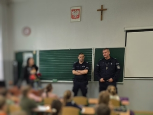 Umundurowani policjanci przeprowadzający prelekcję dla uczniów w szkole.