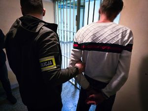 na zdjęciu policjant prowadzi zatrzymanego