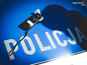 Zdjęcie kolorowe na którym na pokrywie silnika oznakowanego radiowozu Policji znajduje się urządzenie do pomiaru zawartości alkoholu w wydychanym powietrzu. Na pokrywie silnika widnieje napis "Policja".