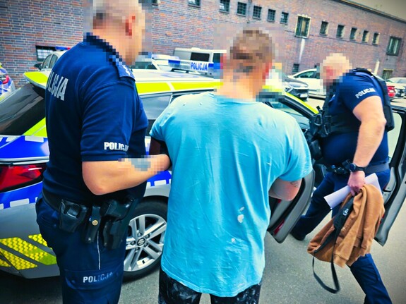 policjanci prowadzą zatrzymanego do radiowozu