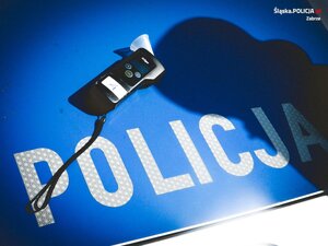 Urządzenie do badania poziomu alkoholu w wydychanym powietrzu, leżące na pokrywie silnika oznakowanego radiowozu Policji.
